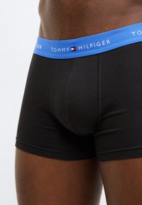 Mustad bokserid sinise elastse vöökohaga, millel on kiri "TOMMY HILFIGER". Sile tekstuur, vormis lõige, kesk-reie pikkus.