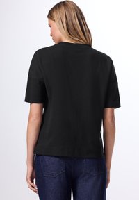 Camiseta corta negra de manga corta con un ajuste relajado, hecha de algodón suave, que cuenta con un cuello redondo y una textura simple y lisa.