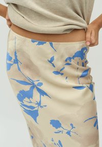 Bloemen midi rok in beige met blauwe bloemenprint. Glad satijnachtige textuur, getailleerd ontwerp en verfijnde taillebanddetails.