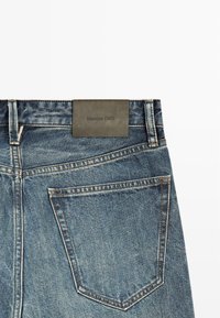 Denim jeans with a medium blue wash, featuring a faux leather label at the waistband and standard back pockets with contrasting stitching.