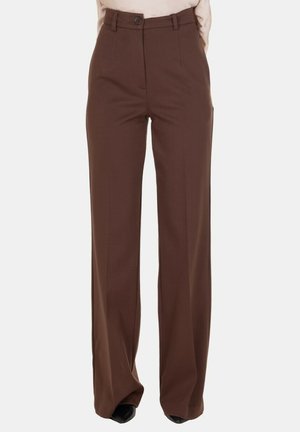 Pantaloni marroni a vita alta a gamba dritta con chiusura a bottone e zip, indossati con un top beige infilato dentro e scarpe nere a punta.