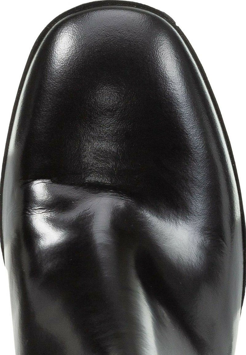 Gros plan sur l'embout d'une chaussure en cuir noir poli, avec une texture lisse et de légères plis à la surface supérieure.