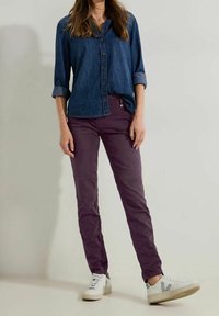 Chemise en denim à boutons, manches longues retroussées ; pantalon slim violet ; baskets blanches avec des accents gris et des semelles texturées.