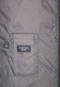 Doublure de veste grise avec une étiquette noire cousue indiquant "CARE LABEL INSIDE" et une étiquette de taille marquée "36" sur le côté gauche.