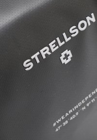 Črn teksturiran material z v embossiranem logotipom "STRELLSON" in simbolom križa; vsebuje hashtag in geografske koordinate v beli barvi.