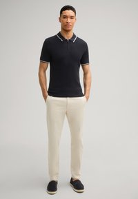 Polo shirt navy con accenti bianchi, maniche corte e colletto con zip, abbinato a pantaloni beige chiaro e espadrillas navy.