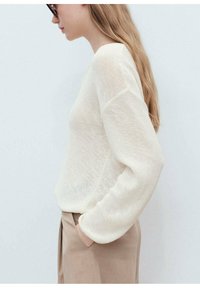 Cream knit sweater with a relaxed fit and long sleeves, paired with brown trousers. Notable texture and lightweight material.