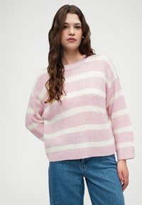 Pulôver de malha listrado em rosa e branco, com um ajuste relaxado, gola redonda e ombros caídos, combinado com jeans azuis. Tecido texturizado.