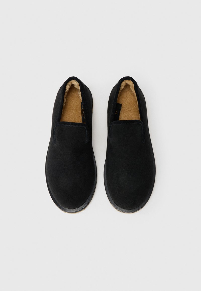 Scarpe slip-on nere con un morbido esterno in suede testurizzato, foderate in pile color cammello e con punta arrotondata, dotate di una suola piana in gomma.