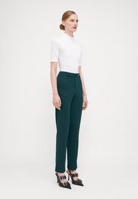 Biele priliehavé tričko s krátkym rukávom, tmavozelené elegantné nohavice s vreckami a čierne lodičky s špicatou špičkou a s prackami.