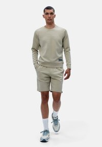 Light beige sweatshirt and shorts set, made of soft cotton blend. Features ribbed cuffs, slight texture, and a small logo patch on the shorts.