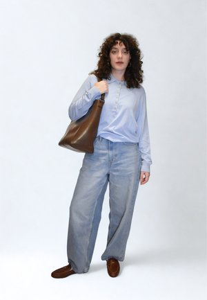 Svetlo modra srajca z dolgimi rokavi in gumbi, kombinirana s širokimi kavbojkami svetle pranja in rjavo usnjeno torbico čez ramo. Rjavi čevlji brez vezalk.