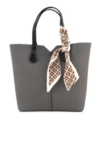 Grijze geweven tote bag met zwarte leren handvatten, met een crèmekleurige sjaal die om een handvat is geknoopt met een bruin geometrisch patroon.
