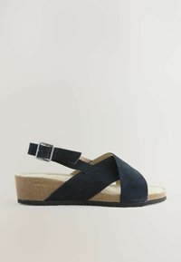 Sandale en daim noir avec un design à brides croisées, boucle autour de la cheville réglable, semelle intermédiaire en liège et semelle extérieure en caoutchouc noir texturé.