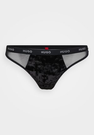 Svart tanga undertøy med fløyelsstruktur, gjennomsiktige mesh-paneler og en merket elastisk midjebånd med "HUGO"-logo i sølv.