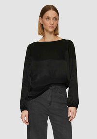 Zwarte blouse met lange mouwen en een relaxte pasvorm, voorzien van een ronde halslijn. Gekocht met grijze jeans met studs op de zakken.