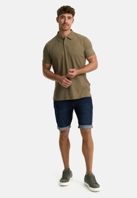 Oliven grøn polo shirt, klassisk krave, korte ærmer; parret med opsmøgede denimshorts og grå sneakers. Casual, tætsiddende design.