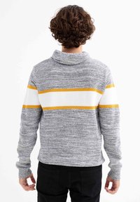 Suéter de punto gris con un alto cuello, que presenta rayas horizontales amarillas y blancas en el pecho y mangas largas con puños acanalados.