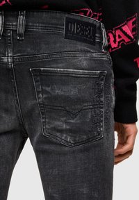 Vaqueros de denim negro con acabado desgastado, que cuentan con un bolsillo trasero, cintura fruncida y una etiqueta de cuero con la marca en la cinturilla.