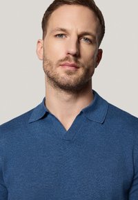 Polówek z niebieskiego dzianiny w serek, z krótkim rękawem, o teksturowanej tkaninie i płaskim kołnierzyku. Bez wzorów ani ozdób.