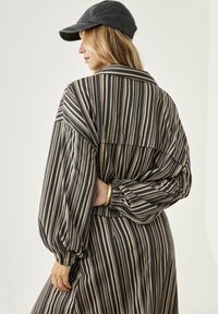 Camisa de manga larga a rayas con cuello y mangas abullonadas en tonos negro y beige, con un detalle fruncido en la parte posterior.