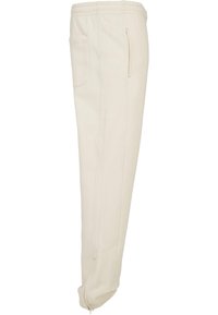 Pantaloni jogger de crem deschis, cu talie elastică, două buzunare laterale și manșete cu fermoar. Realizați dintr-un material moale, texturat.