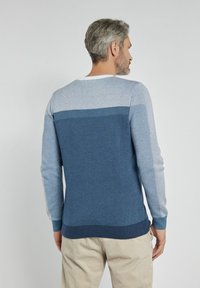 Męski sweter z teksturowanym splotem w różnych odcieniach niebieskiego, z okrągłym dekoltem oraz ściągaczami przy rękawach i u dołu. Neutralne spodnie dopełniają stylizację.