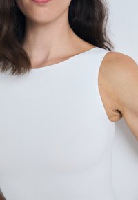 Bijela bezramena bodi izrađen od glatkog, rastezljivog materijala s suptilnim, urezanim logotipom Calvin Klein na prednjoj strani.