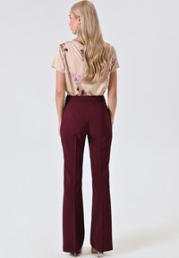 Vloeiende beige blouse met bloemenpatronen, gecombineerd met aansluitende bordeauxrode flarebroek. Zachte textuur, elegante val en minimalistisch design.