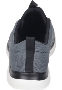 Grå idrottssko med en texturerad ovandel, svart inredning och vit sula. Utrustad med en tygöglan bak för enkel påtagning.