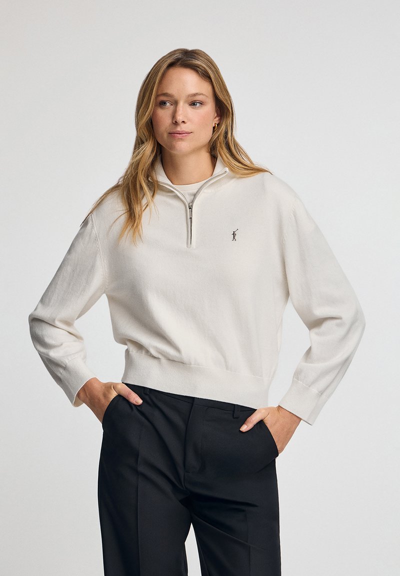 Cremfarbener Pullover mit einem Halbzip-Kragen, gerippten Bündchen und Saum; verfügt über ein kleines, dunkles gesticktes Logo auf der Brust.