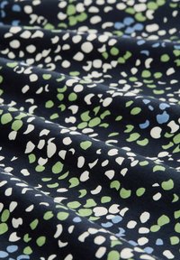 Laivastonsininen kangas, jossa on hajallaan valkoisia, vihreitä ja vaaleansinisiä muotoja, pehmeällä tekstuurilla ja hieman kiiltävällä pinnalla.