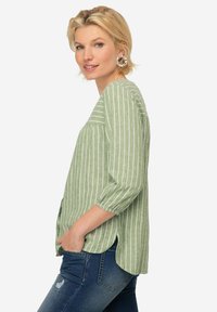 Blusa verde a rayas con mangas tres cuartos, detalle fruncido en los hombros y dobladillo redondeado. Fabricada en tejido ligero.