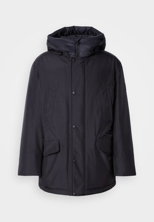 Veste matelassée noire avec une capuche amovible, présentant des fermetures à bouton, deux grandes poches avant et un extérieur lisse et résistant à l'eau.