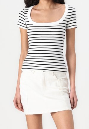 Femme portant un haut ajusté à manches courtes rayé horizontalement blanc et noir et une mini-jupe en denim blanc avec poches.