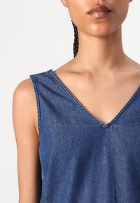 Top de ganga sem mangas com decote em V. O tecido é azul escuro e apresenta um acabamento suave e texturizado com detalhes de costura visíveis.