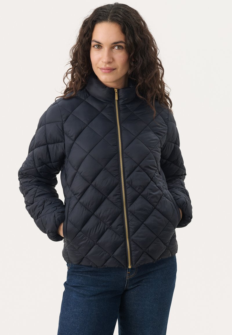 Jachetă matlasată de culoare bleumarin, cu guler înalt, fermoar auriu și buzunare laterale. Prezintă un finisaj texturat cu un model geometric în formă de diamant.