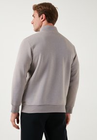 Sudadera gris claro con cuello alto, mangas largas y puños de canalé. Tejido suave con una textura lisa y un diseño sencillo.