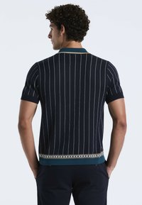 Marineblauwe polo met korte mouwen en verticale witte strepen. Bevat een turquoise kraag en een decoratieve patroonrand aan de onderkant. Gemaakt van textuurstof.