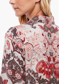 Blusa fluida con un motivo floreale in rosso, nero e bianco. Tessuto a costine con colletto classico e dettagli di design intricati.