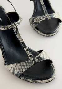 Sandali alti con stampa di serpente in bianco e nero, dotati di cinturini incrociati e una suola nera liscia, caratterizzati da un delicato design con cinturini.