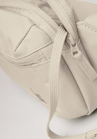 Borsa beige con zip realizzata in tessuto testurizzato, dotata di più scomparti e una tracolla intrecciata. Logo stampato sul lato.
