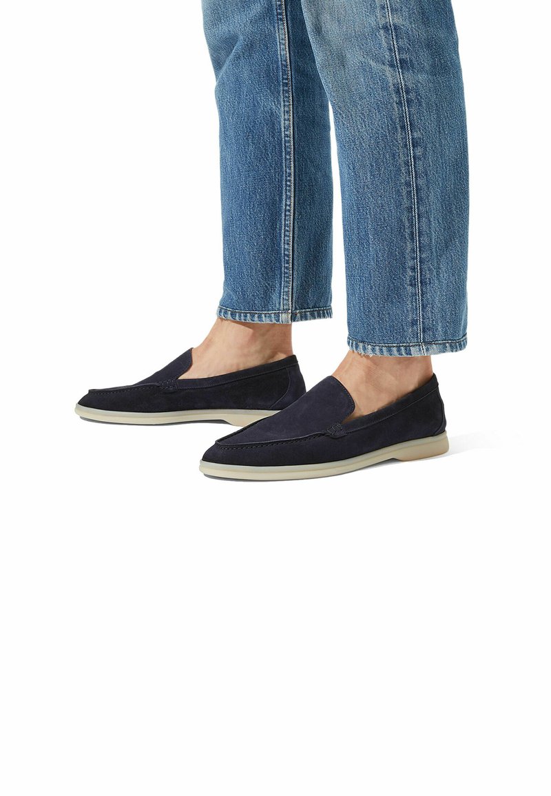 Zapatos de ante azul marino de tipo slip-on con un diseño de perfil bajo y suelas de goma beige. Presentan detalles de costura en la parte superior y una textura suave.