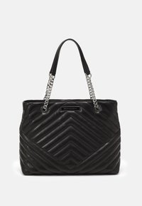 Czarna pikowana torba typu tote z wzorem w jodełkę, z sylwetkowymi uchwytami złożonymi z srebrnych łańcuchów oraz czarnym skórzanym paskiem na ramię. Z przodu umieszczona jest plakietka z logo.