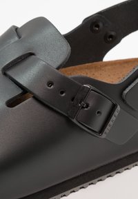 Black leather sandal with two adjustable straps, a buckle, and a textured cork insole. Contoured footbed and rubber sole with a serrated edge.
