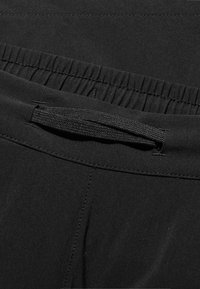 Black fabric waistband with elastic gathering and a dark woven drawstring. Smooth texture and minimal stitching details.