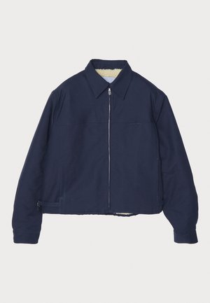 Veste bleu marine avec fermeture éclair à l'avant, col pointu et intérieur doublé. Elle présente un design court et des poches zippées sur les côtés.