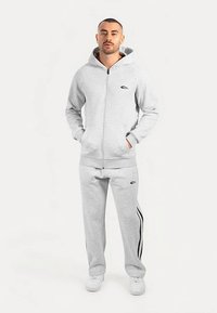 Grauer Kapuzenpullover mit Reißverschluss und Logo, passende Jogginghose mit schwarzen Seitenstreifen und weiße Turnschuhe. Lässige Sportbekleidung aus weichem Stoff.