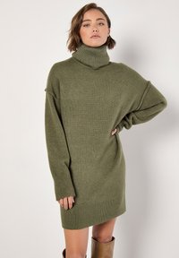 Vestido suéter de cuello alto de gran tamaño en verde oliva con puños y dobladillo acanalados, que cuenta con una textura suave y un corte relajado.