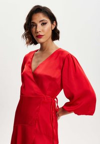 Red satin wrap dress featuring a deep V-neck, puff sleeves, and a tie waist, with a smooth texture and a flowing design.
